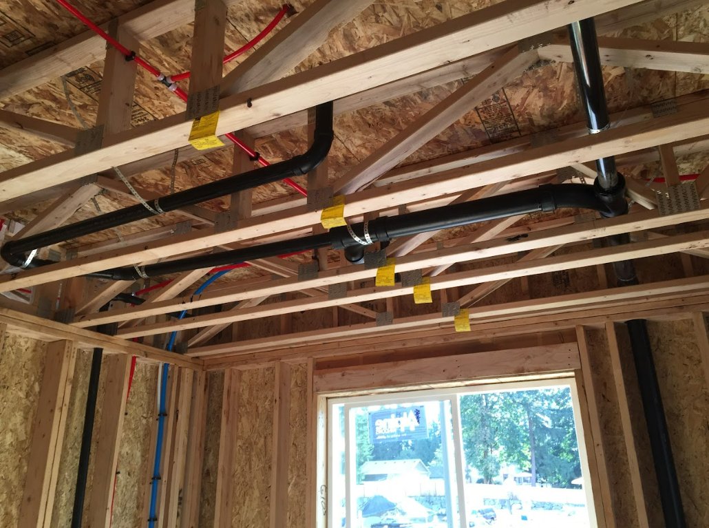 ABS drain line and red and blue PEX supply runs through the floor trusses of a new build