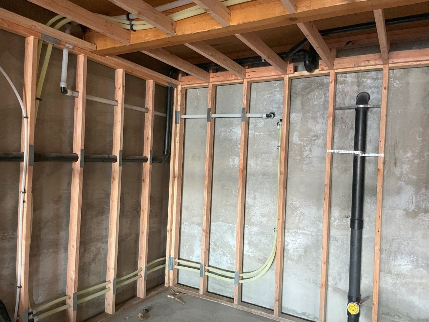 PEX supply and ABS drain lines roughed in on new framing against a concrete basement wall