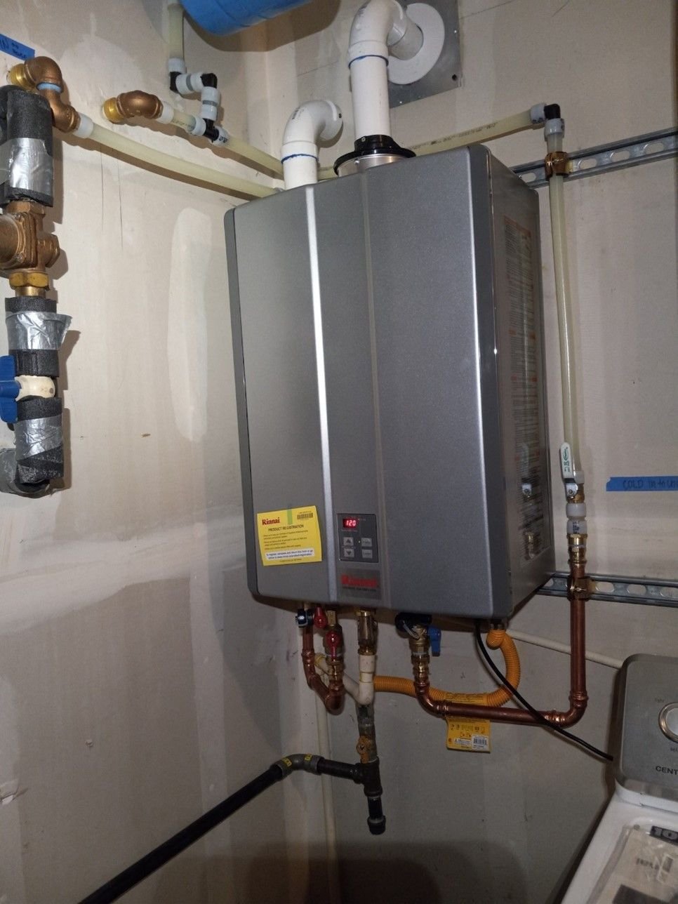 Wall-mounted tankless water heater with copper, PEX and gas connections in a utility room